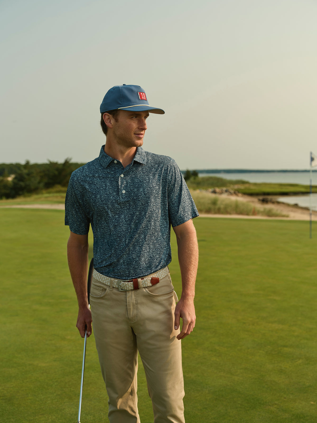 Man wearing a blue heathered polo shirt on a golf course with water views behind him.