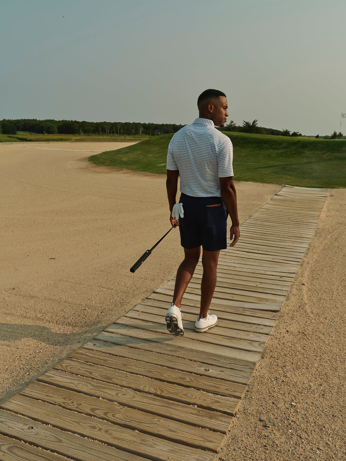 Man wearing a light blue and white striped polo shirt on a golf course holding a golf club.