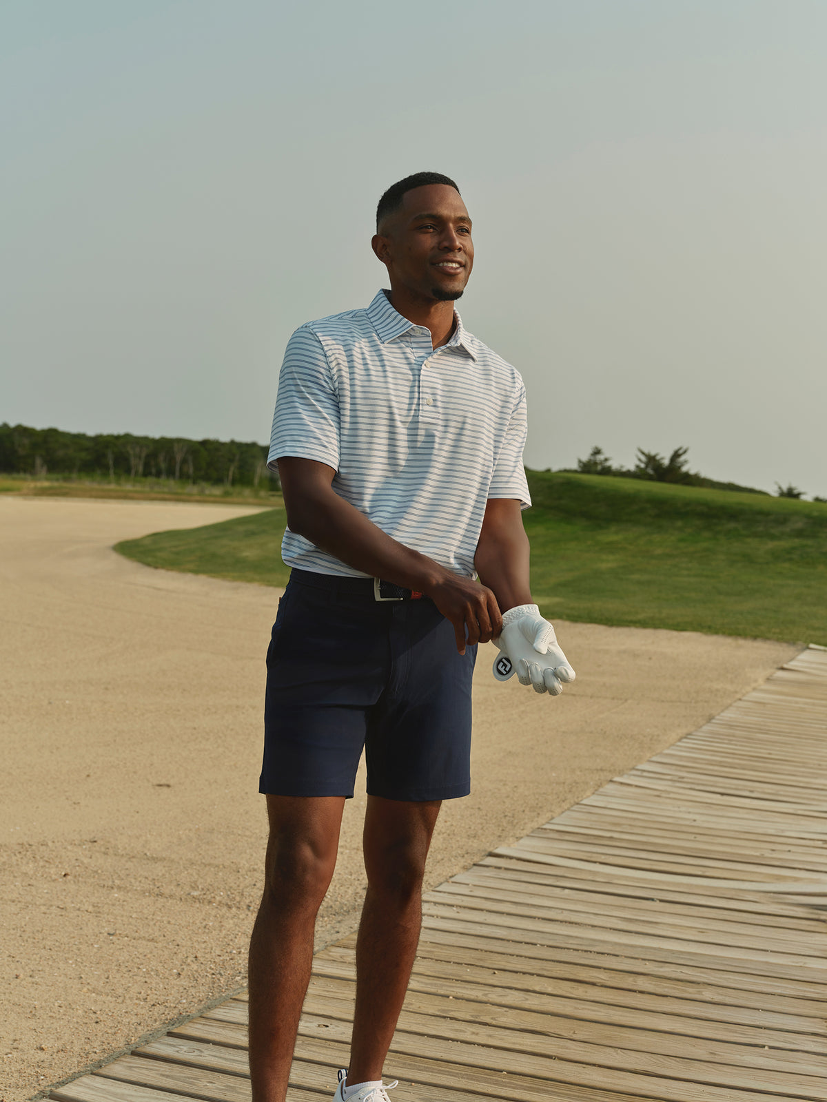 Man wearing blue and white striped polo shirt standing on golf course boardwalk.
