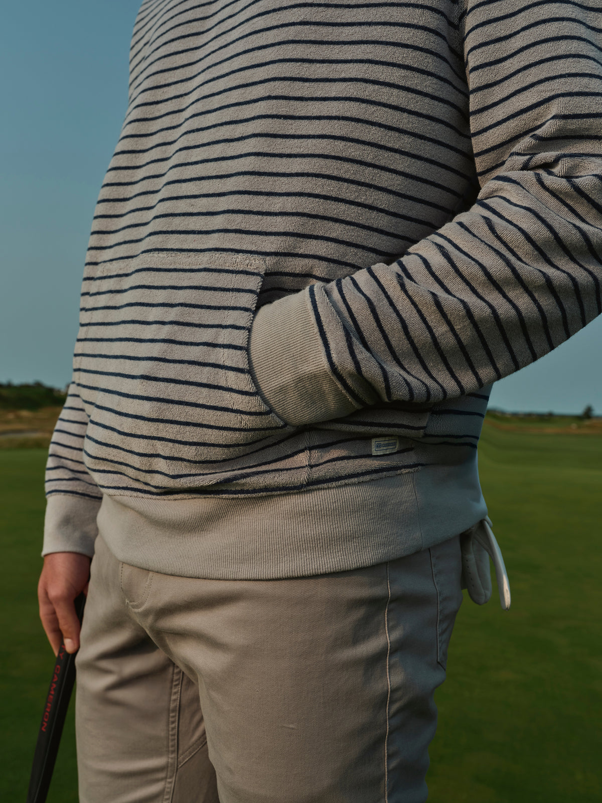 Beige and navy striped terry hoodie worn with khaki pants in an outdoor setting.