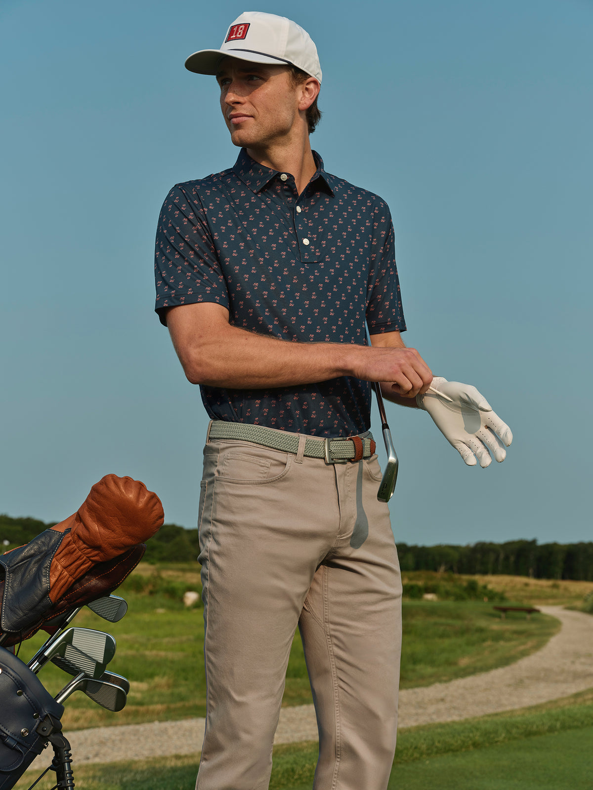 Man wearing navy patterned polo shirt with khaki pants and white cap on golf course.