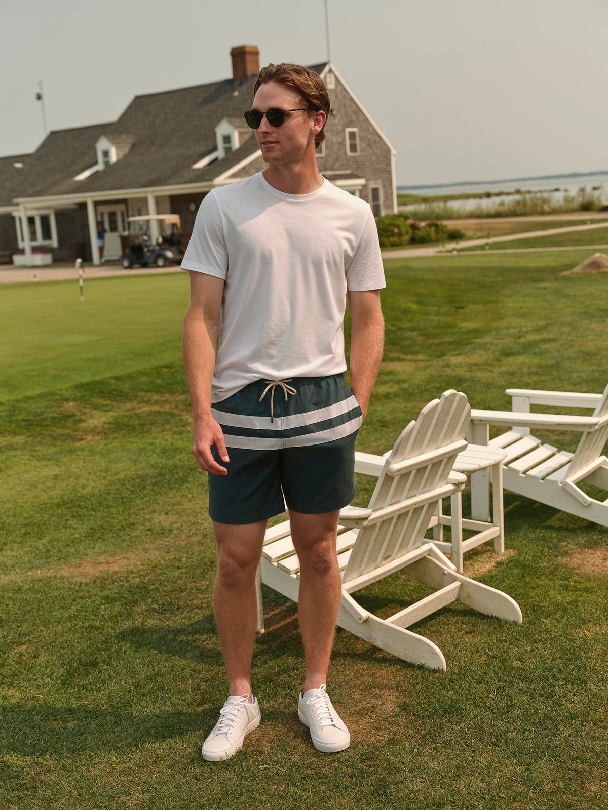 Man wearing white t-shirt and fairway green swim trunk with stripe detail standing on lawn.