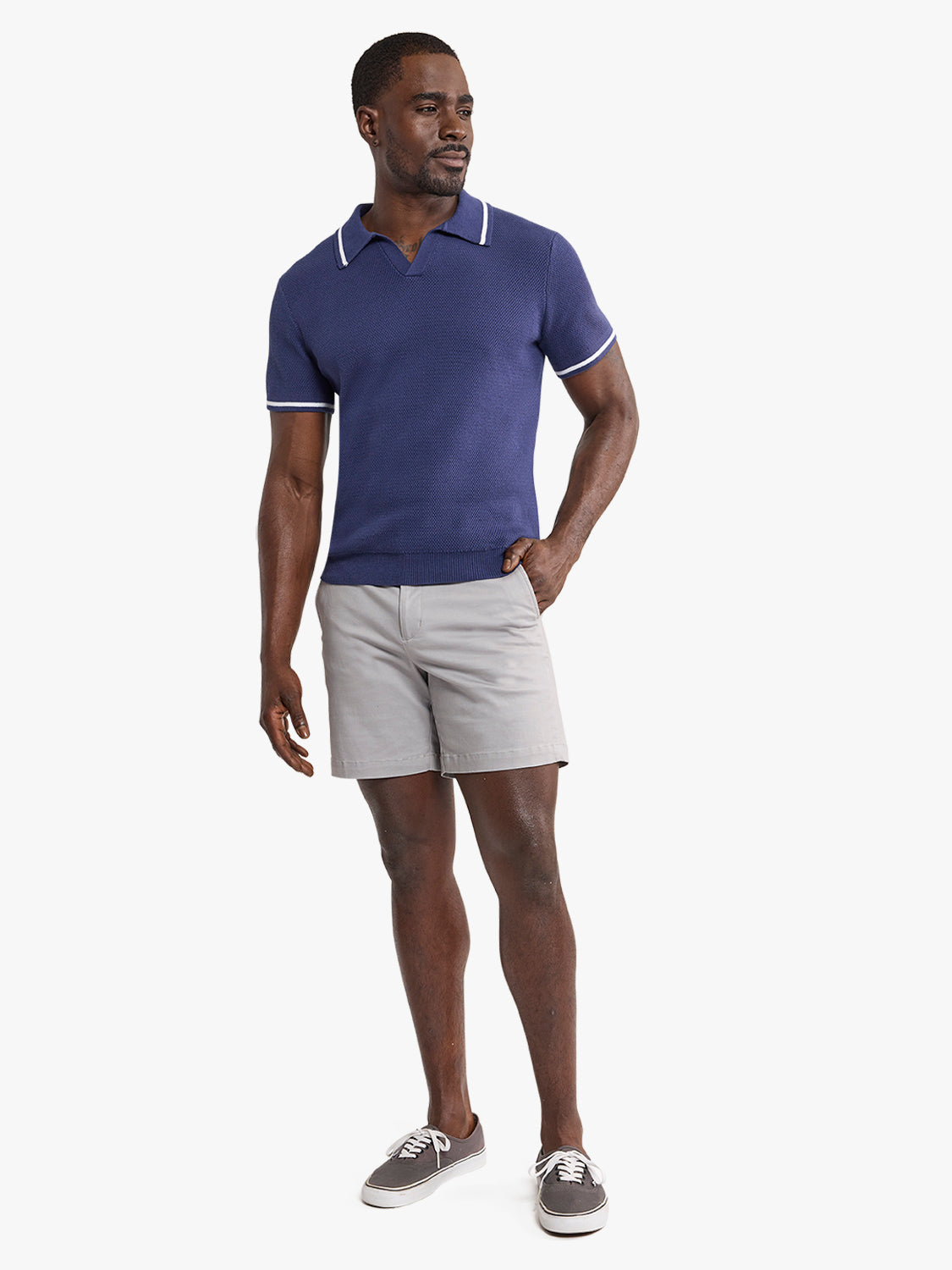 Man wearing a navy polo shirt with white trim and light gray shorts standing against a white background.