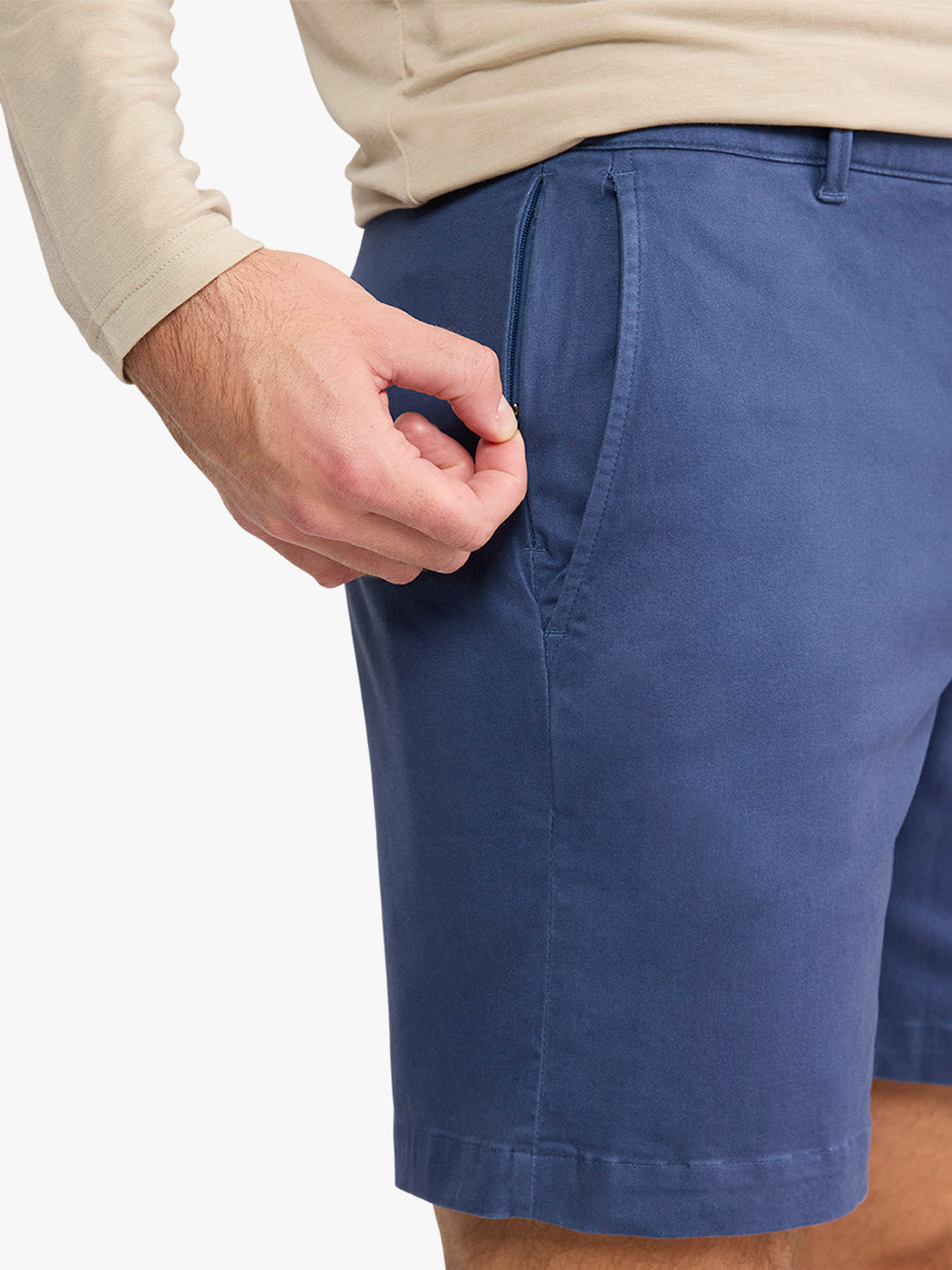 Man wearing navy blue shorts with a beige long-sleeved shirt, showing front pocket detail.