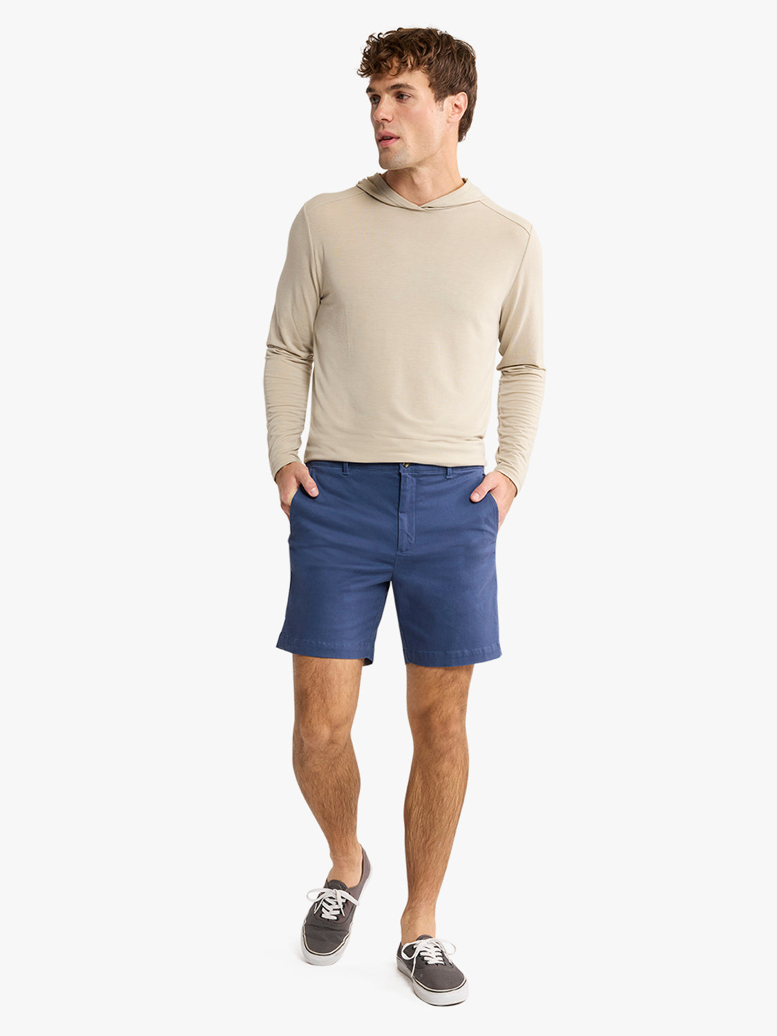 Man wearing navy blue shorts with a beige long-sleeved hoodie and dark sneakers.