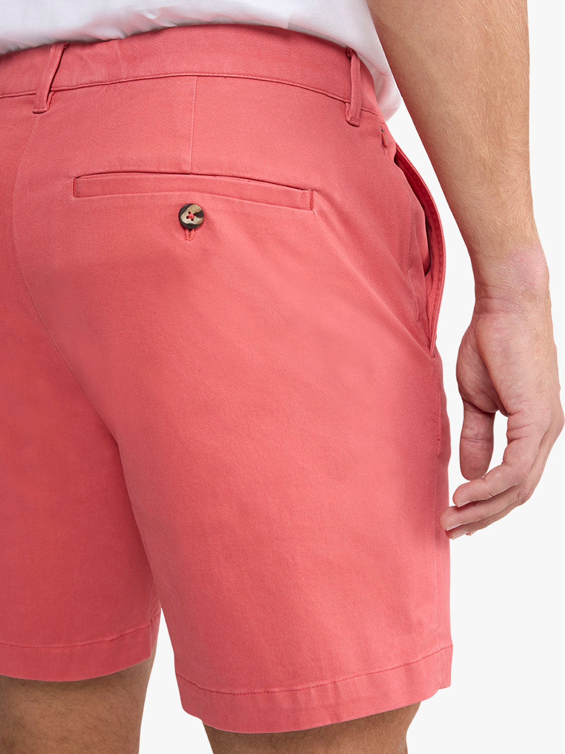 Man wearing washed red shorts with front pockets and decorative button detail on thigh.