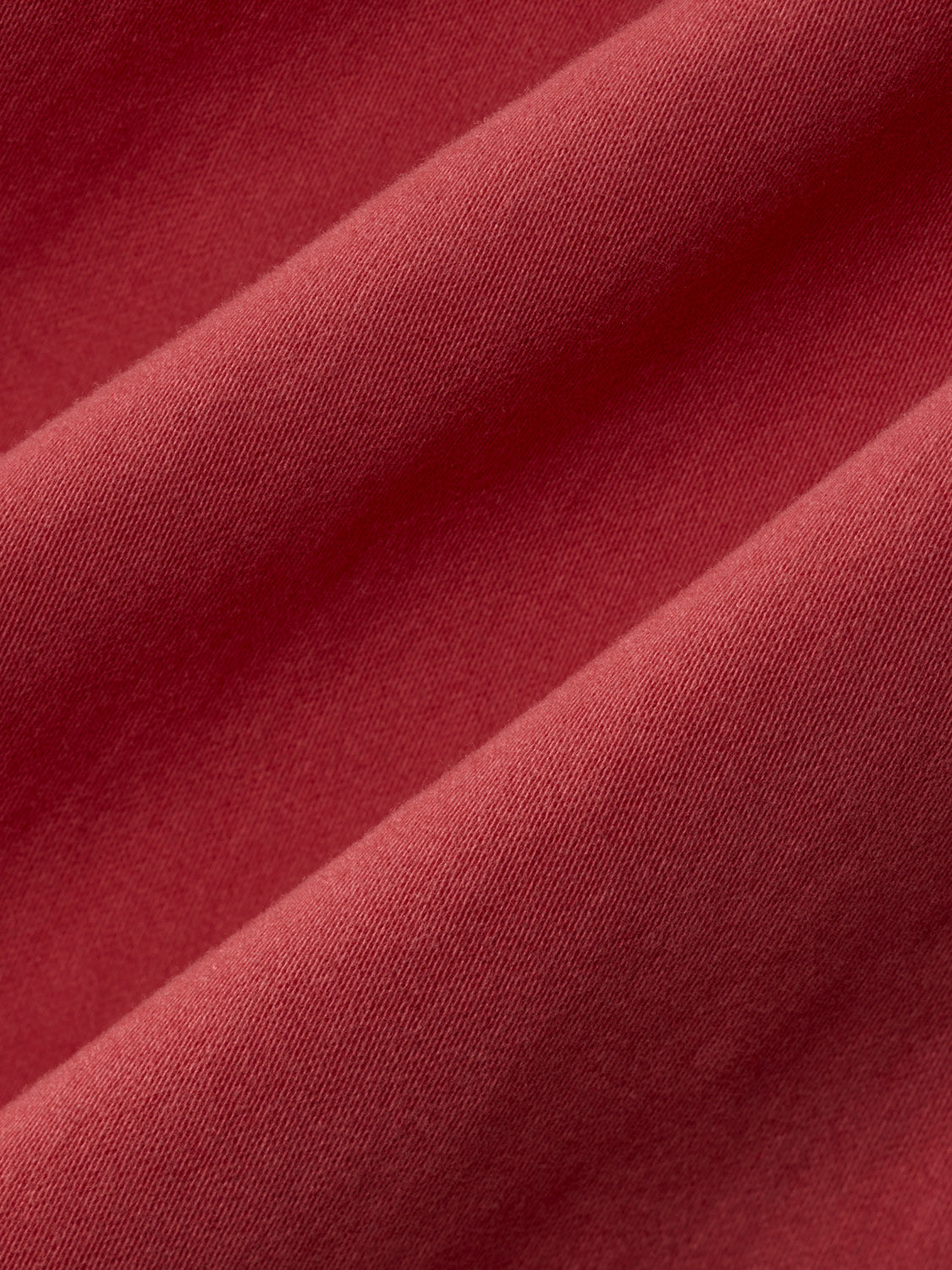 Washed red ribbed fabric with diagonal folds and shadows showing texture and depth.