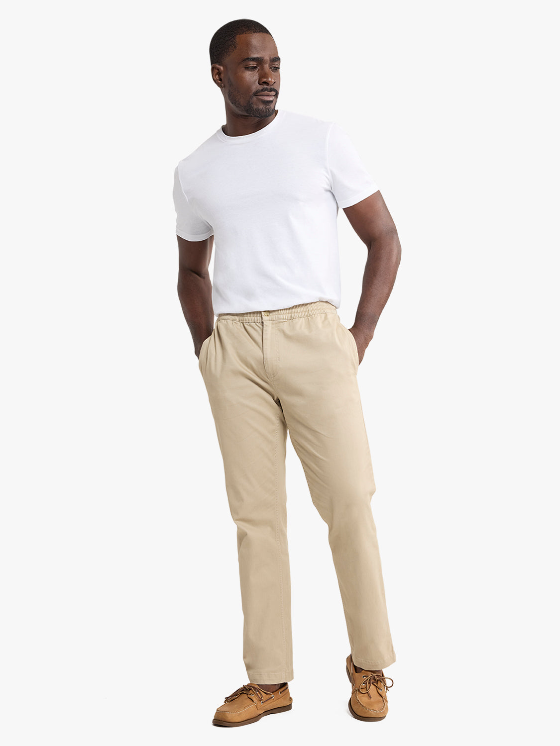 Man wearing a white t-shirt and khaki pull-on pants with hands in pockets.