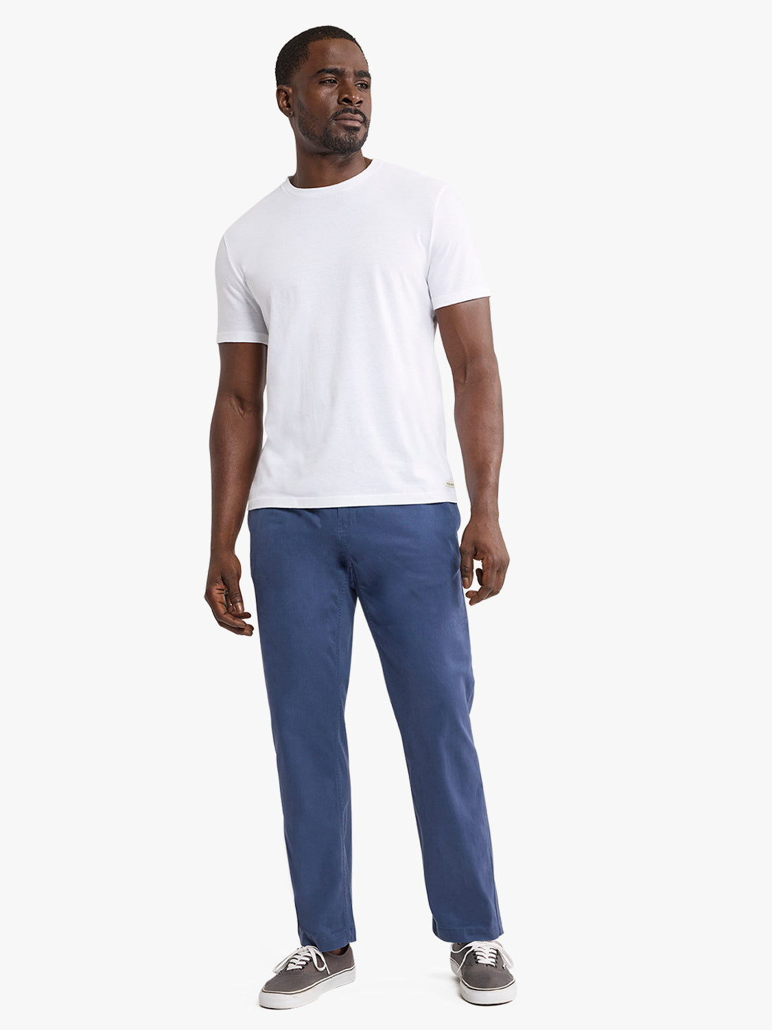 Man wearing white short-sleeve t-shirt and navy pull-on pants with gray sneakers.