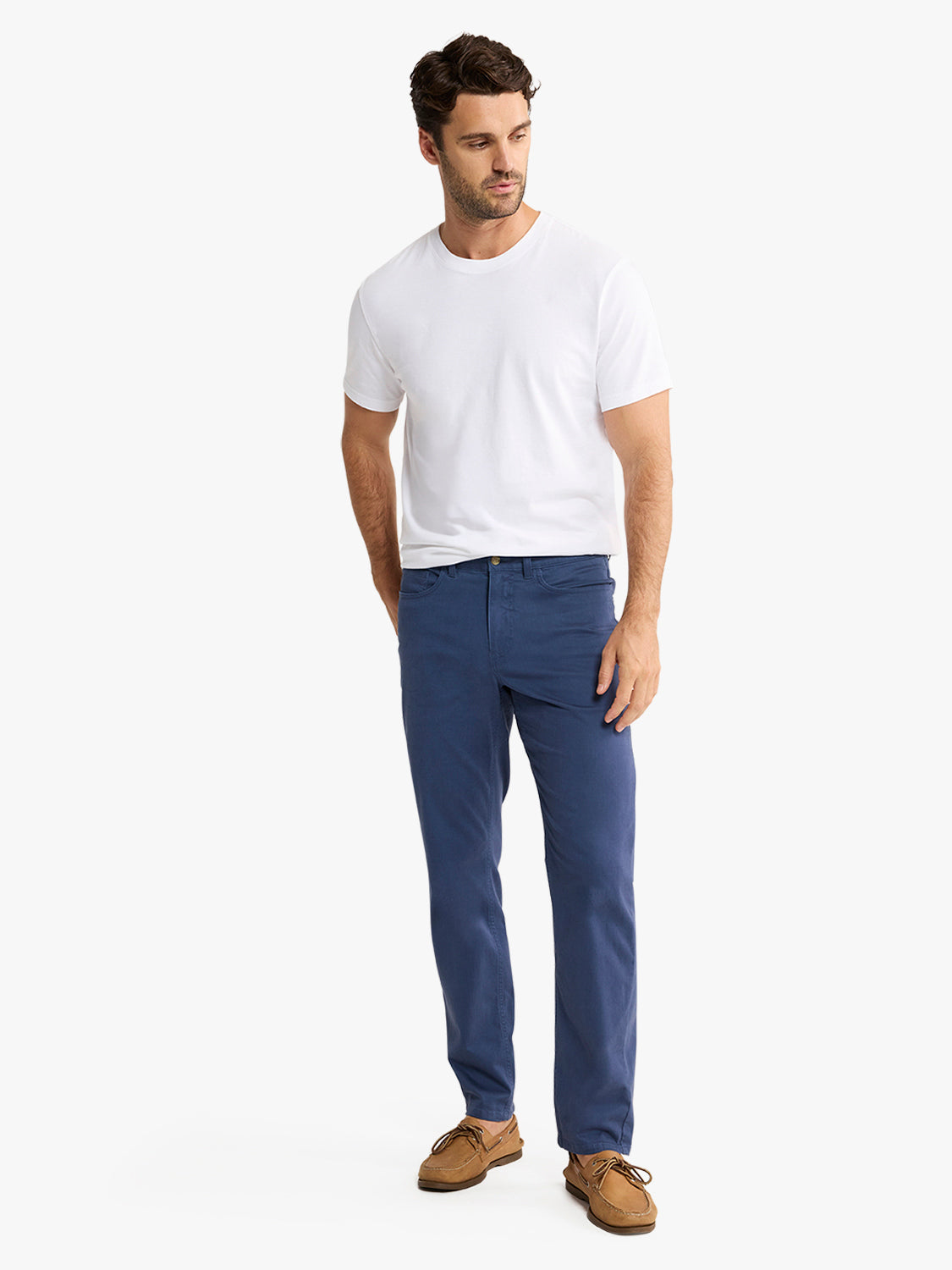 Man wearing a white short-sleeve t-shirt and navy blue five-pocket pants with brown shoes.