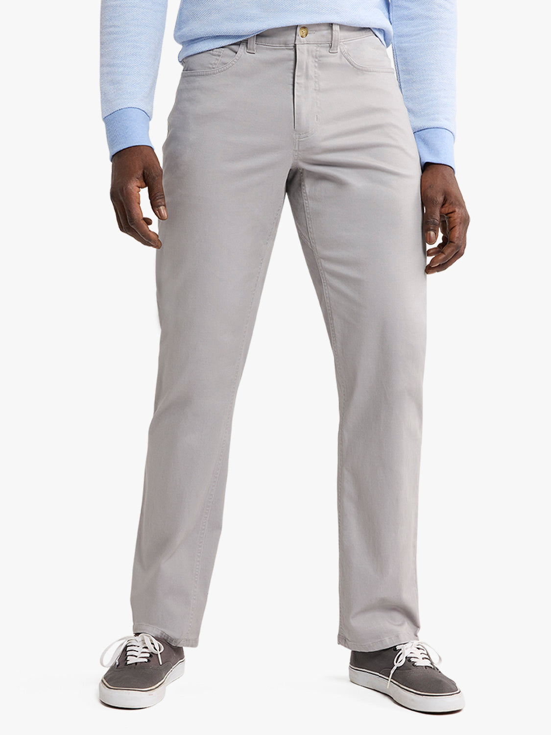 Man wearing light gray five-pocket pants with a blue long-sleeve shirt and gray sneakers.