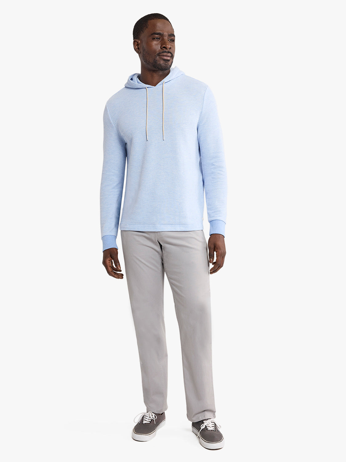 Man wearing a light blue hoodie and seastone-colored five-pocket pants with casual sneakers.