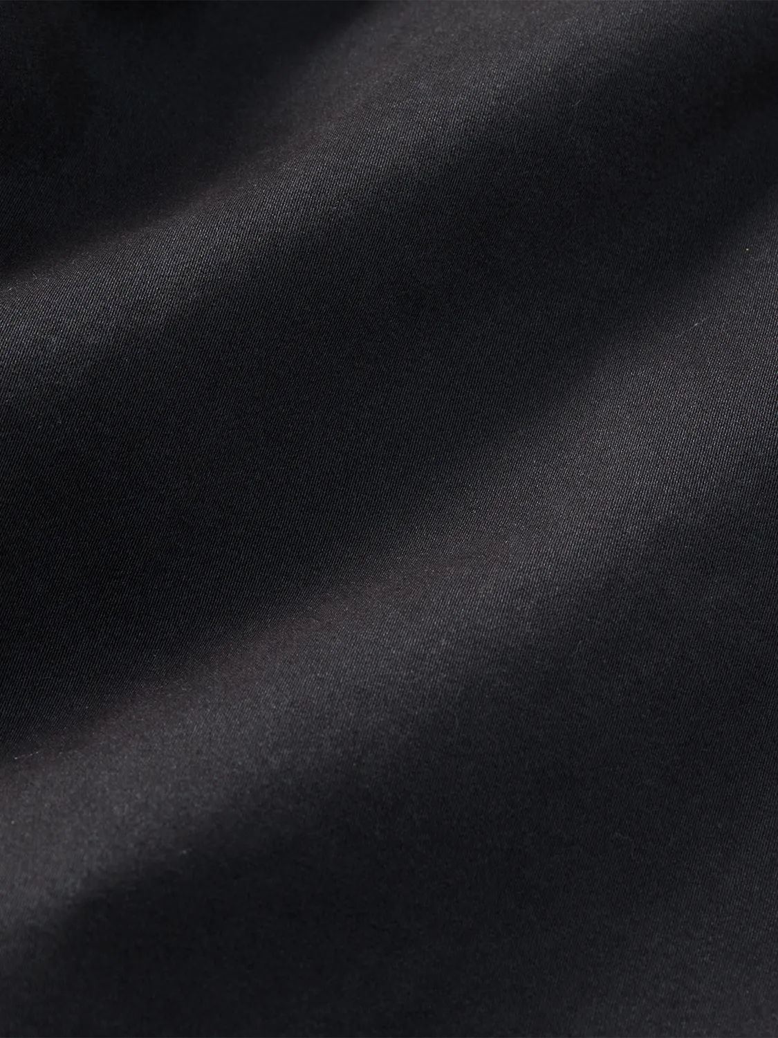 Black pants fabric with diagonal seams and a smooth woven texture under natural lighting.