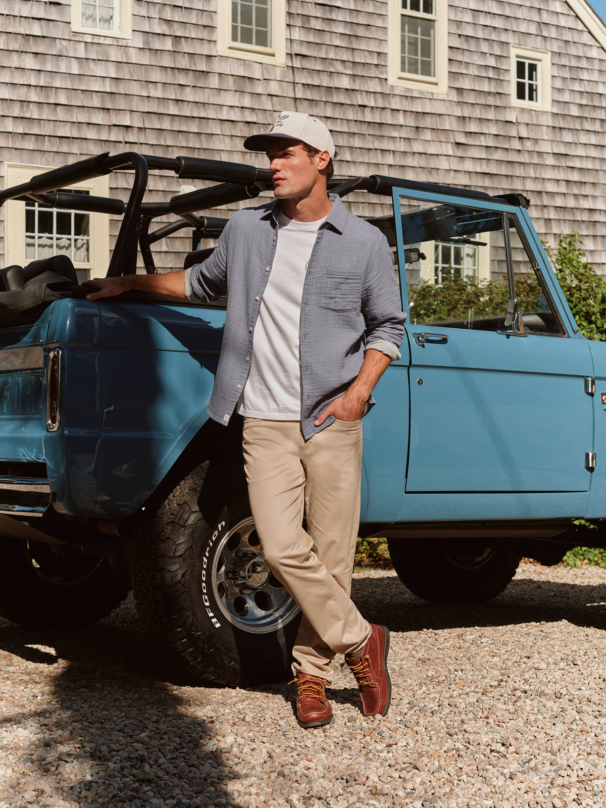 Man wearing khaki five-pocket pants and gray shirt leaning against blue vintage truck.