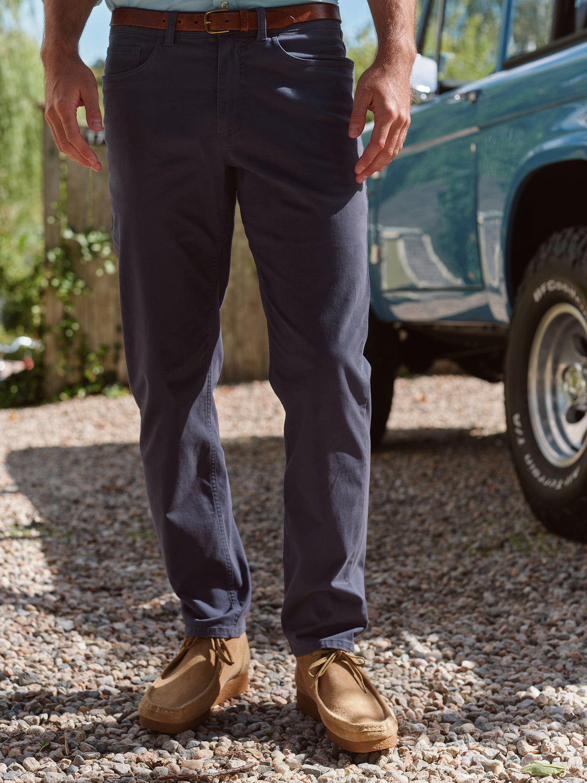 Man wearing navy five-pocket jeans with brown belt and tan boots outdoors.