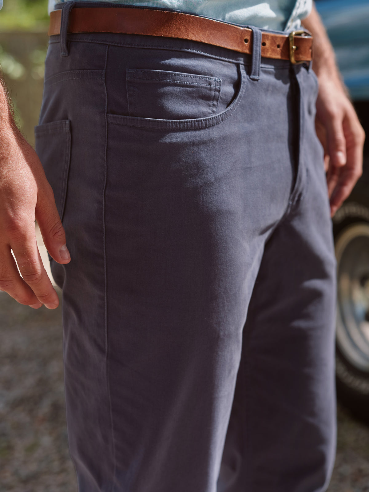 Navy five-pocket pants worn with a brown leather belt, showing front pocket and waistband detail.