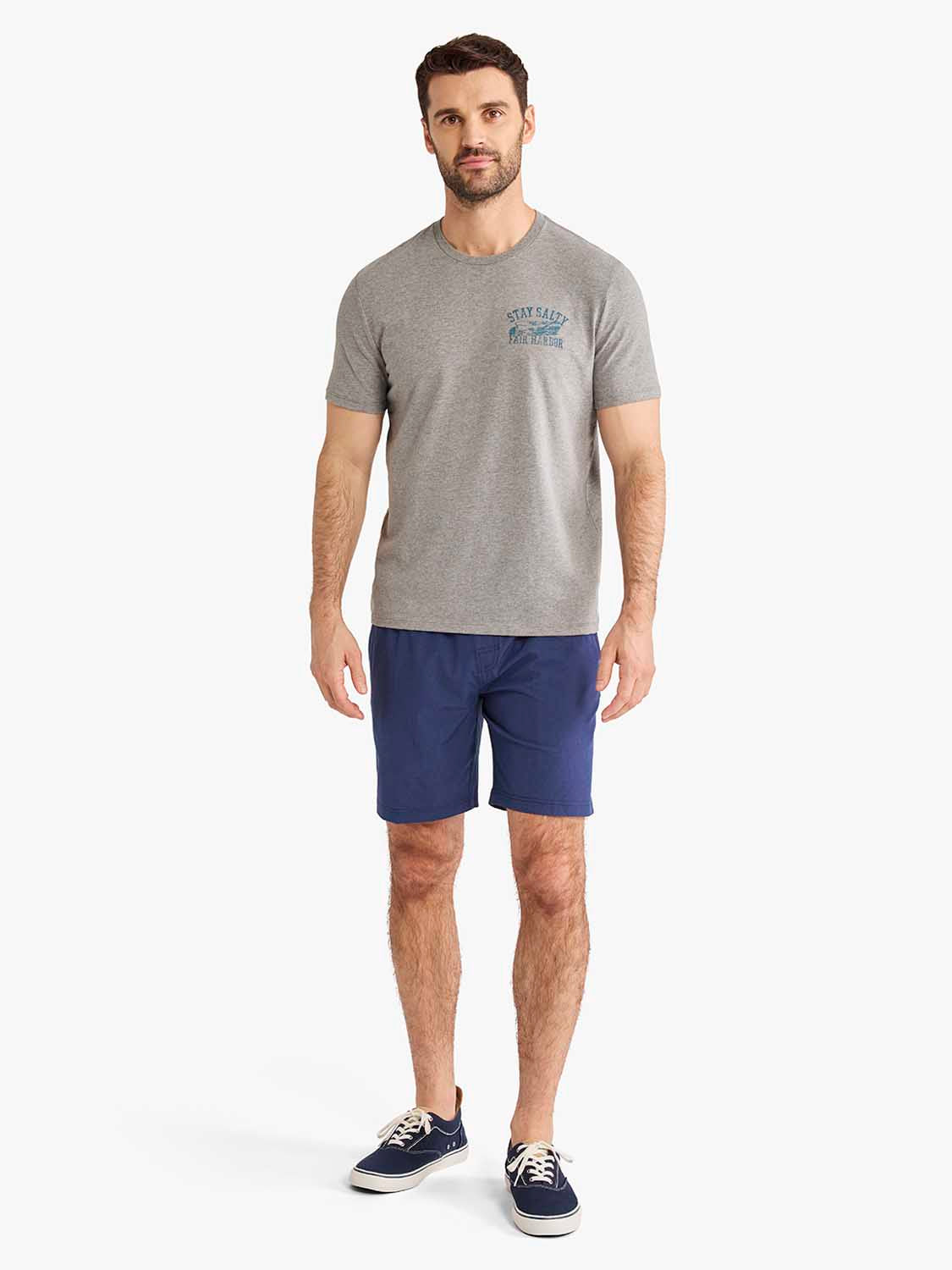 Man wearing heather grey graphic tee with boat adventure design and navy shorts.