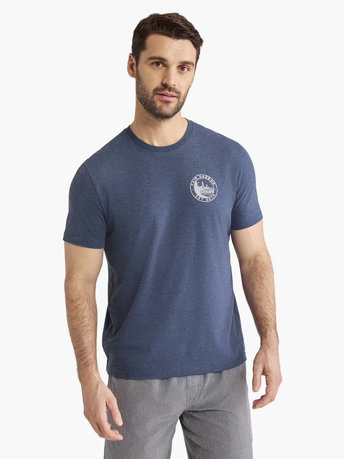 Man wearing a blue-heathered crew neck t-shirt with a circular lighthouse stamp graphic on the chest.
