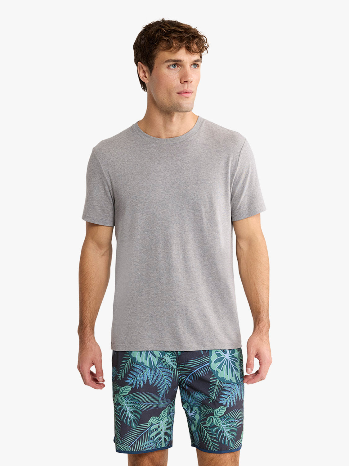 Man wearing a heather grey short-sleeved crewneck tee with tropical patterned shorts.