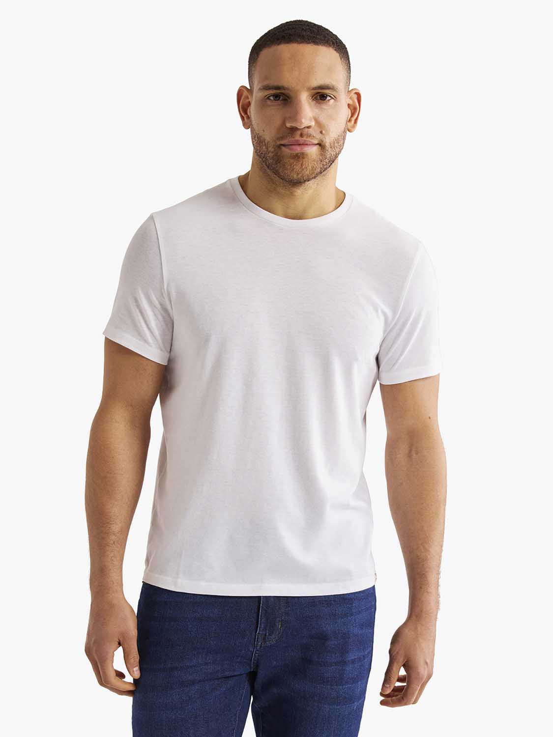 Man wearing a white crew neck short-sleeve t-shirt paired with dark blue jeans.