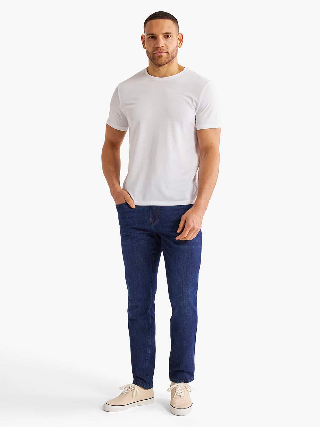 Man wearing a white crew neck t-shirt with dark blue jeans and beige canvas shoes.