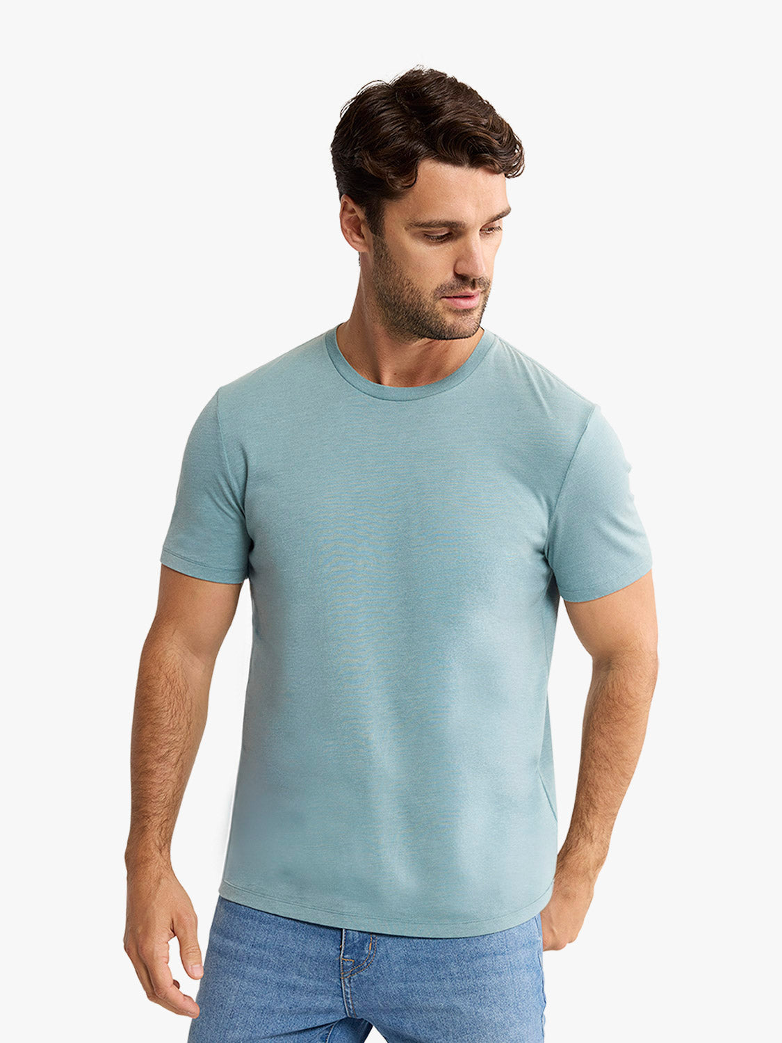 Man wearing a heather green crew neck t-shirt with short sleeves and blue jeans.