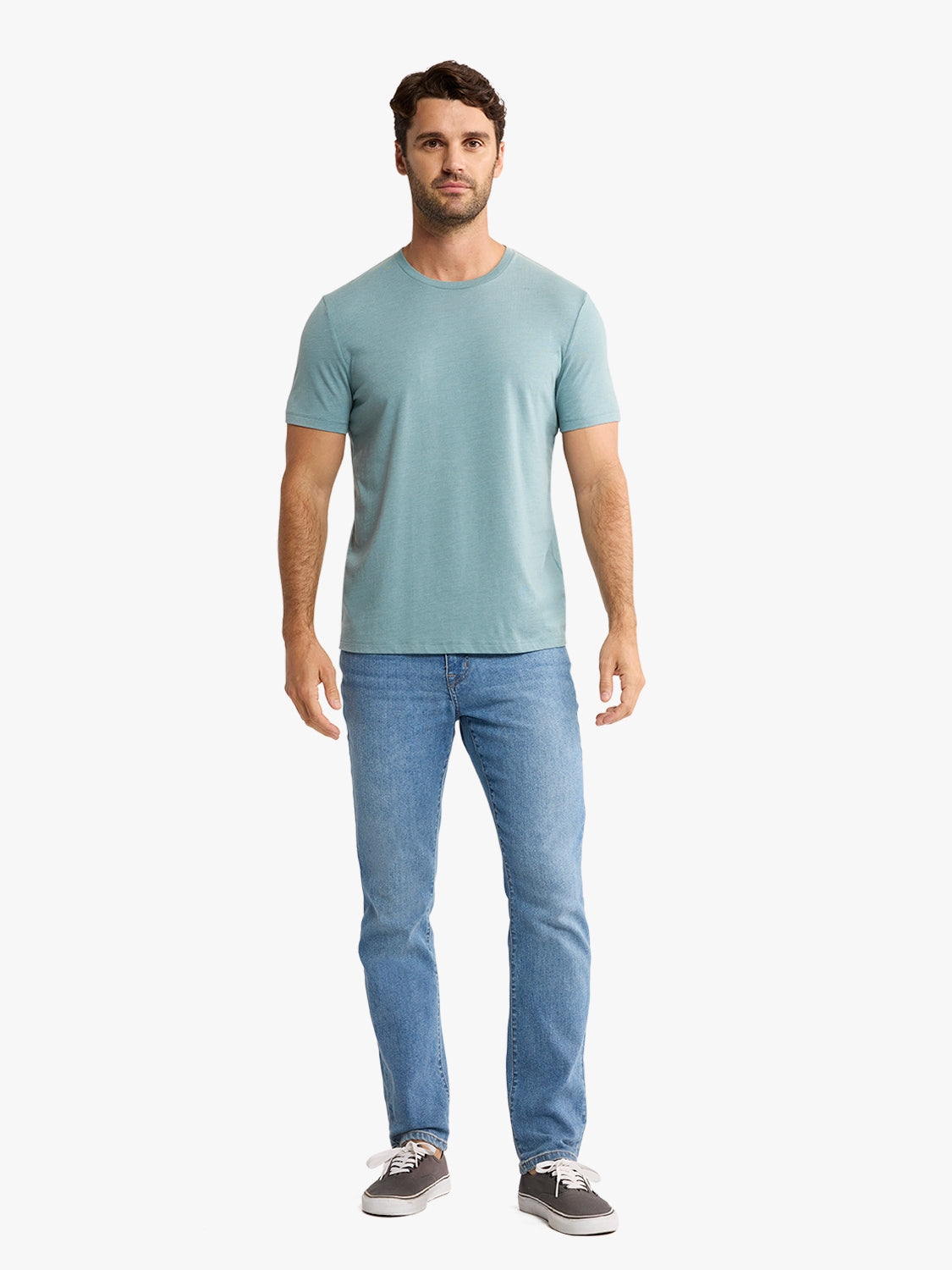 Man wearing a heather green short-sleeve t-shirt with blue jeans and gray sneakers.