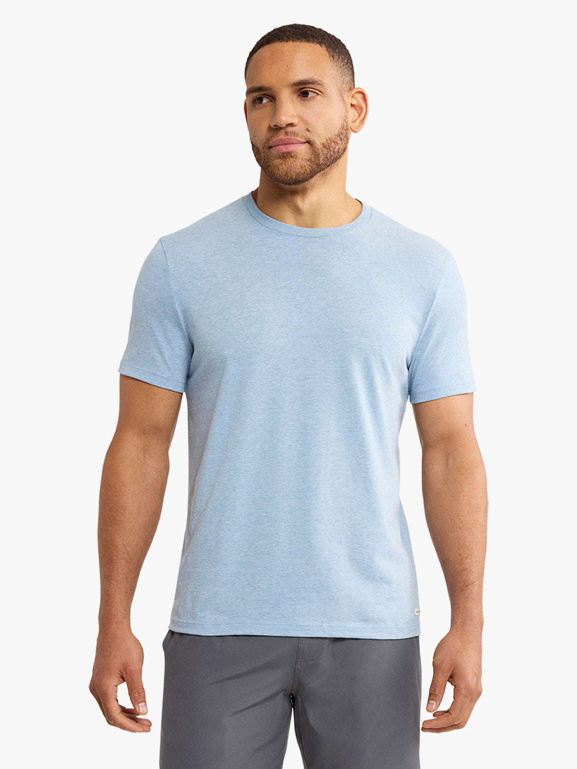Man wearing a light blue faded denim crewneck t-shirt with short sleeves and gray shorts.
