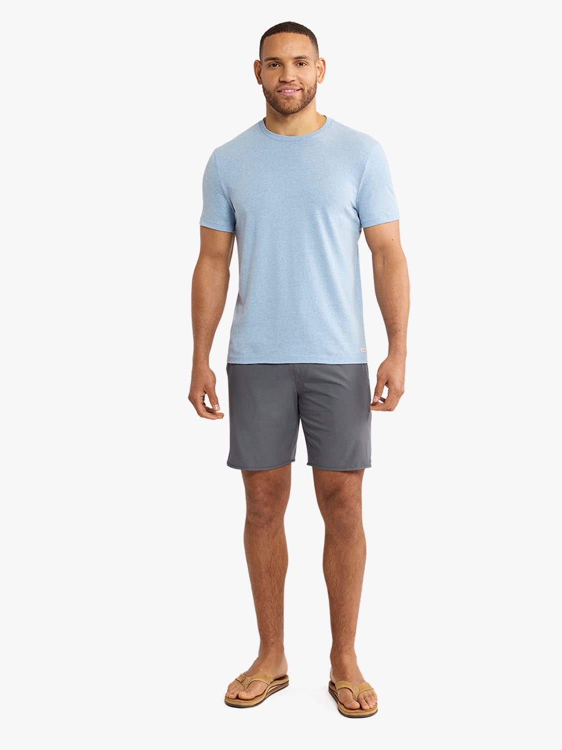 Man wearing a light blue short-sleeve crew neck t-shirt with gray shorts and tan sandals.
