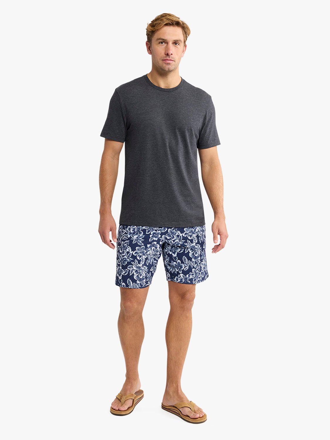 Man wearing a dark gray short-sleeved crew neck t-shirt with patterned shorts and sandals.