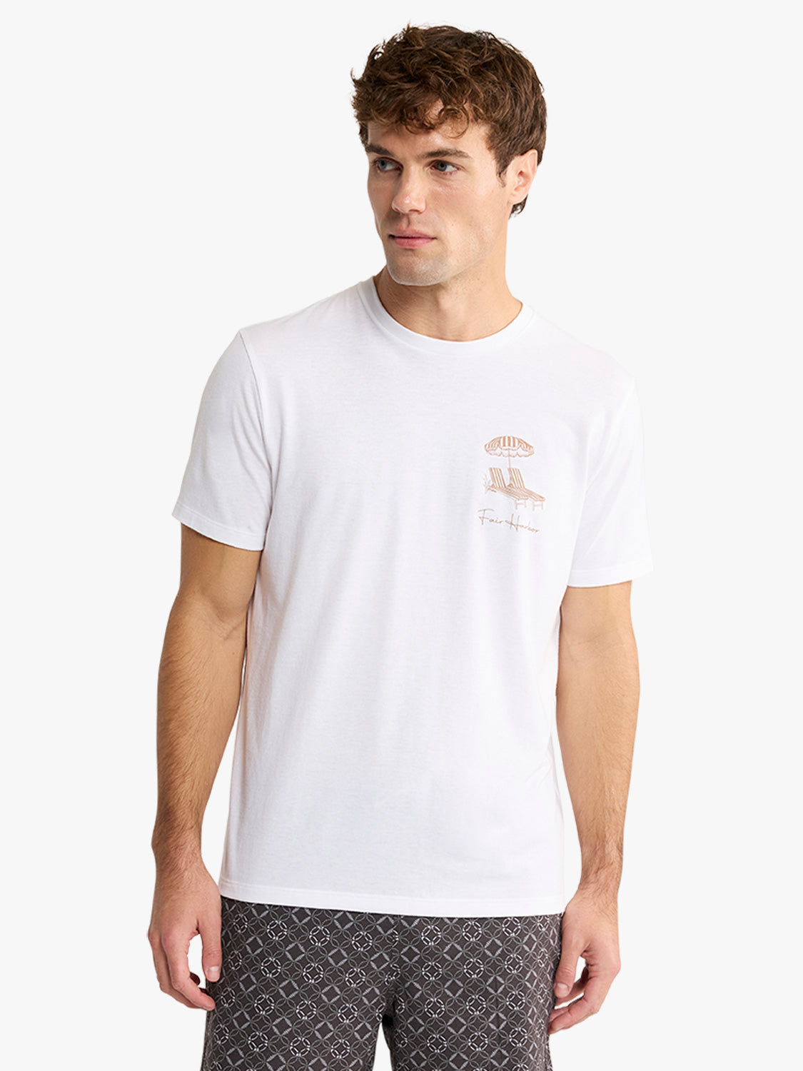 Man wearing a white graphic tee with a small beach umbrella and chair design on the chest.