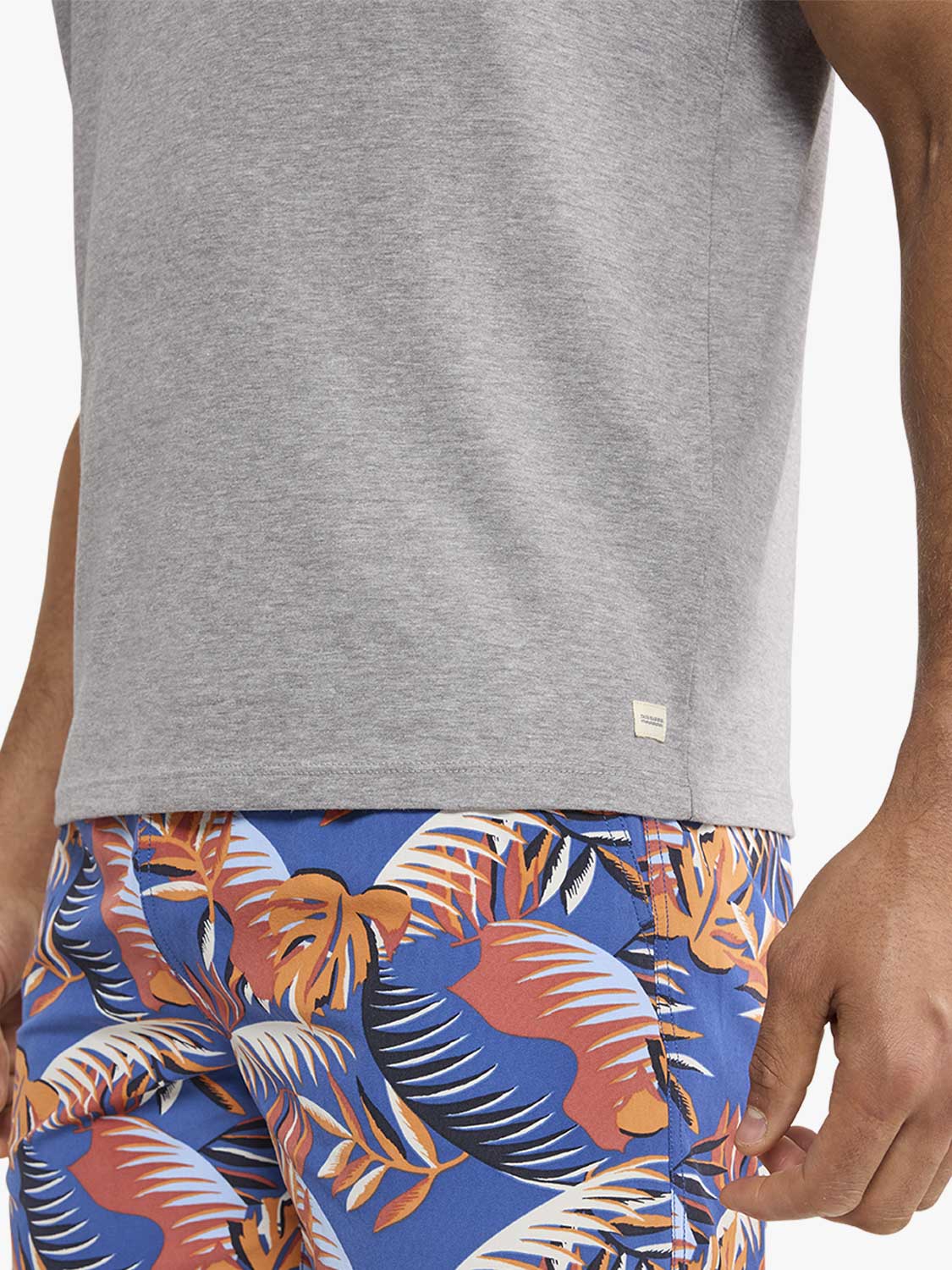 Gray short-sleeve t-shirt with small brand label worn with colorful tropical patterned swim shorts.