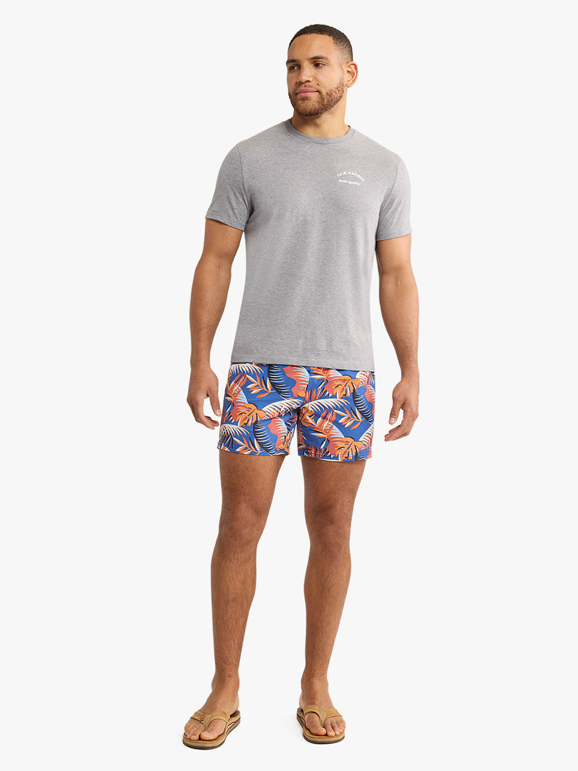 Man wearing gray graphic tee with small chest print and tropical patterned swim shorts.