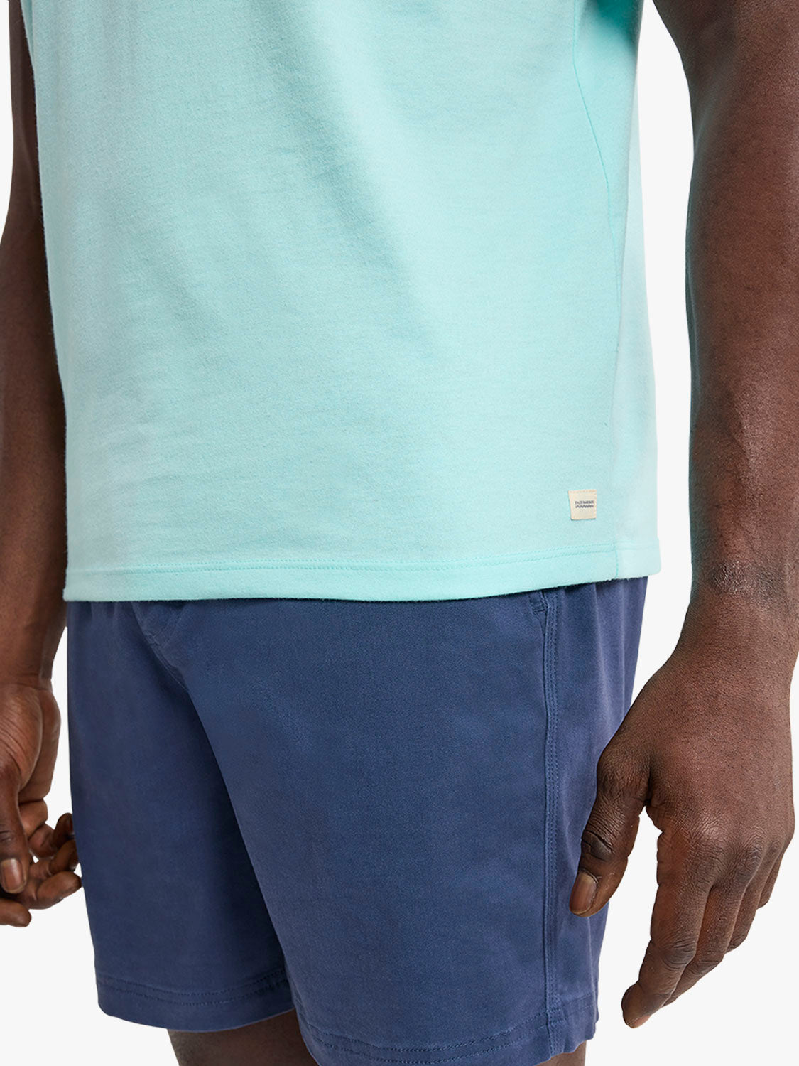 Person wearing an aqua colored short-sleeve t-shirt with a small rectangular label on the front.