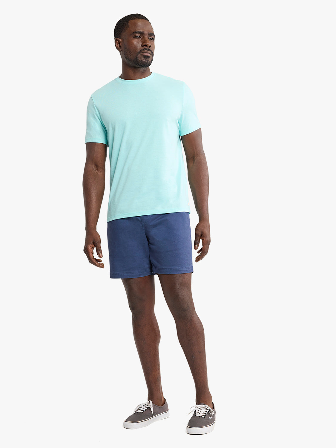 Man wearing an aqua crew neck short-sleeve t-shirt with navy shorts and gray canvas sneakers.
