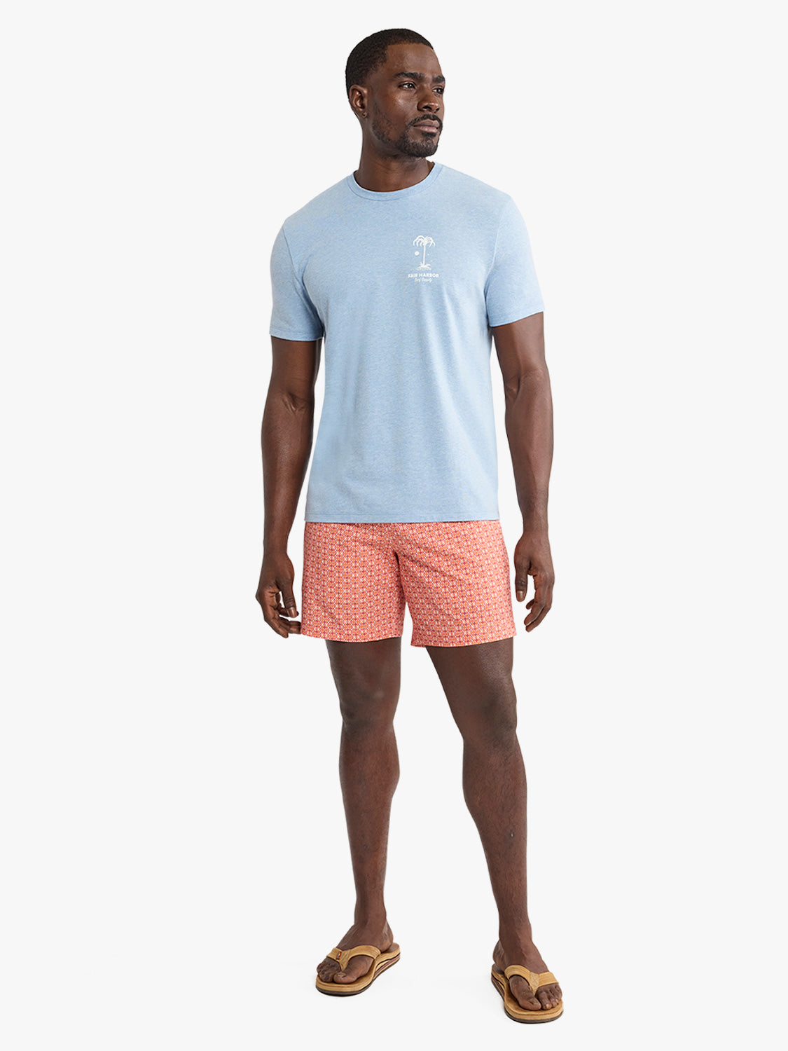 Man wearing light blue graphic t-shirt with small palm print and coral patterned shorts.