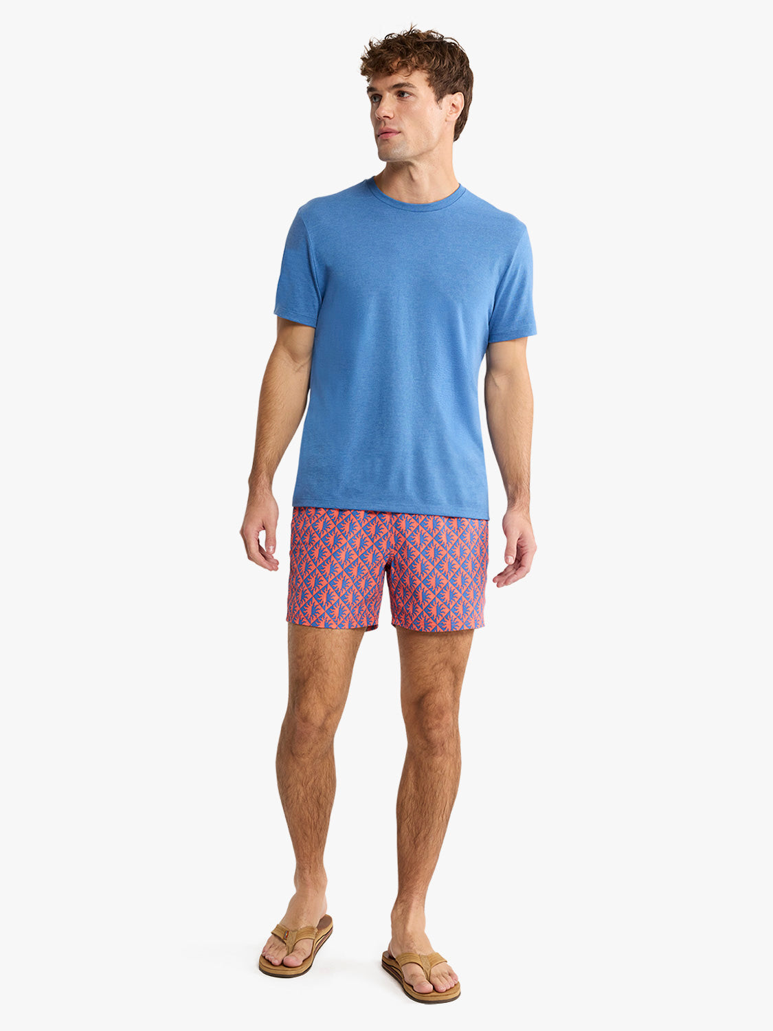 Man wearing a sea blue crewneck t-shirt with patterned shorts and slide sandals.