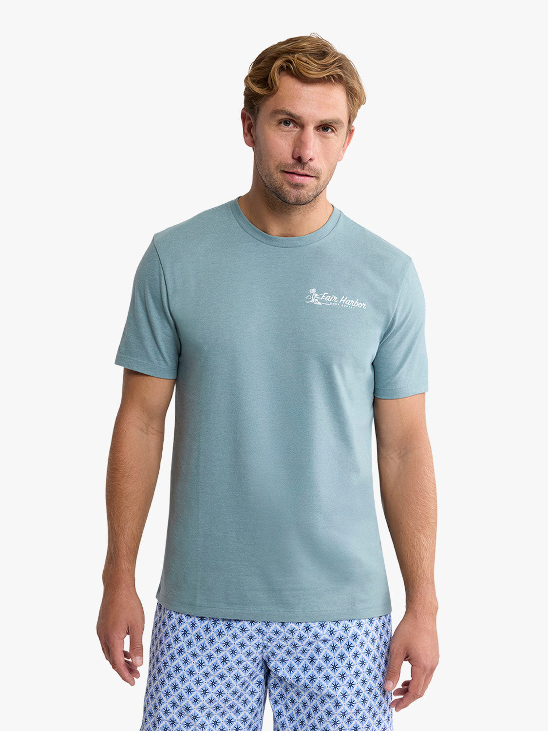 Man wearing a light blue short-sleeve graphic tee with small white chest print and patterned shorts.