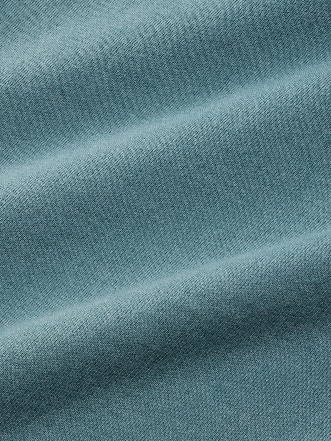 Dusty blue-green graphic tee with diagonal ribbed texture and subtle shading throughout the fabric.