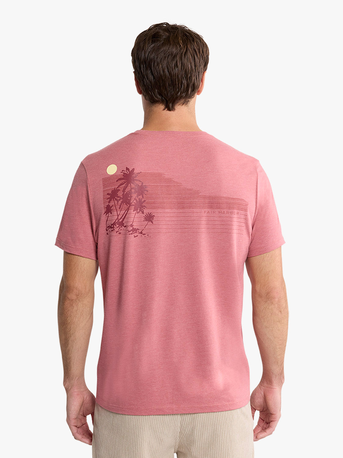 Man wearing a mauve pink t-shirt with a palm tree graphic and moon design on the back.