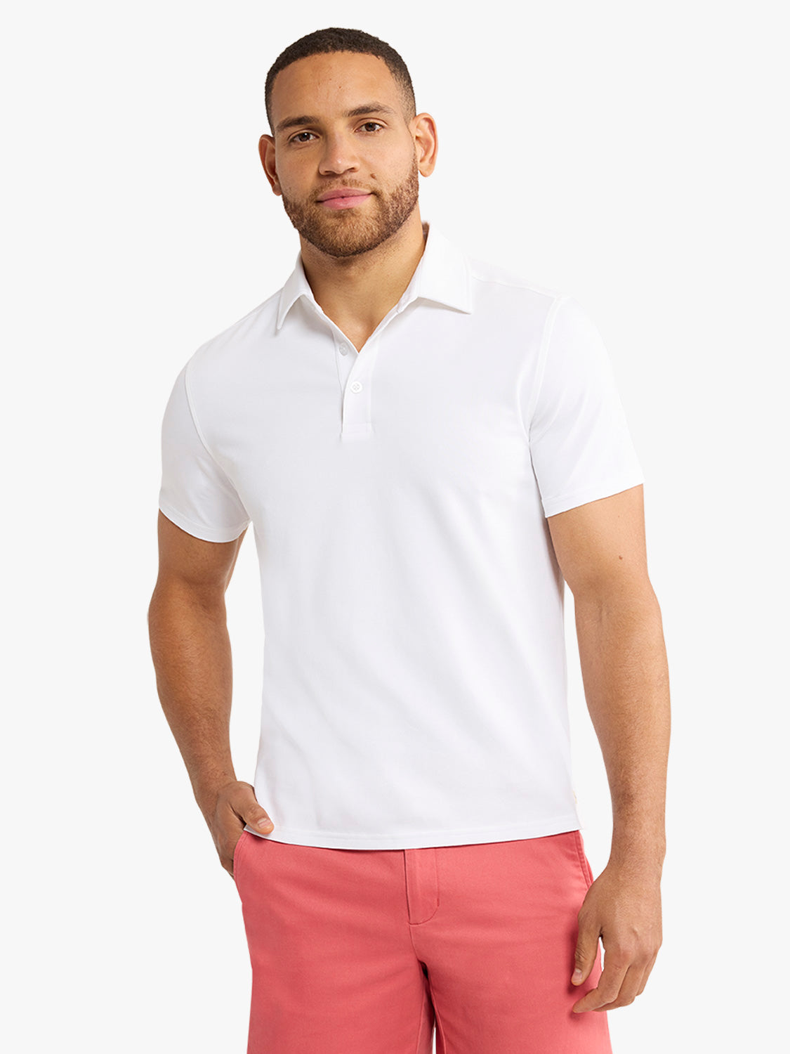 Man wearing a white short-sleeved polo shirt with a chest pocket and coral pink shorts.