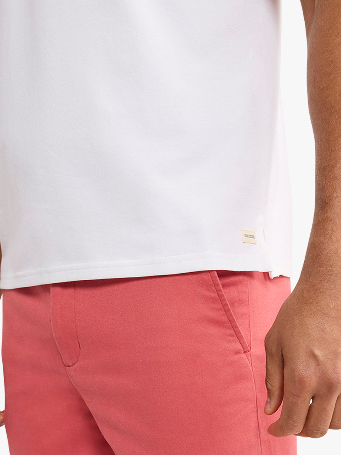 White polo shirt worn with coral pink shorts on a man with brown skin tone.