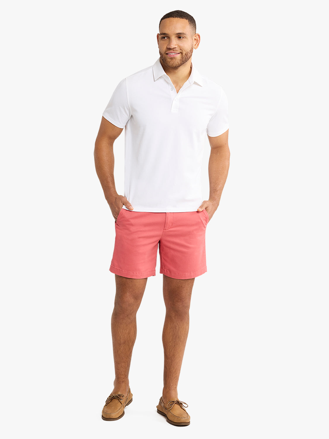 Man wearing a white short-sleeve polo shirt with coral pink shorts and tan boat shoes.