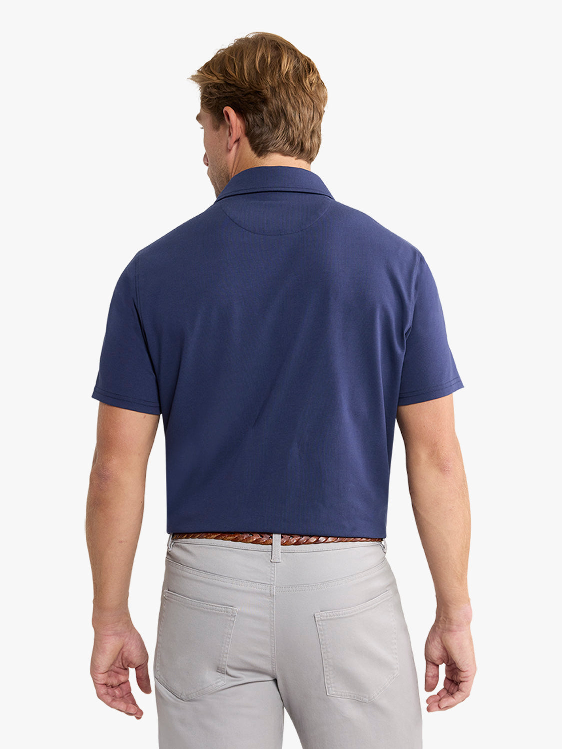 Man wearing navy short-sleeved polo shirt with collar and light gray pants, shown from behind.