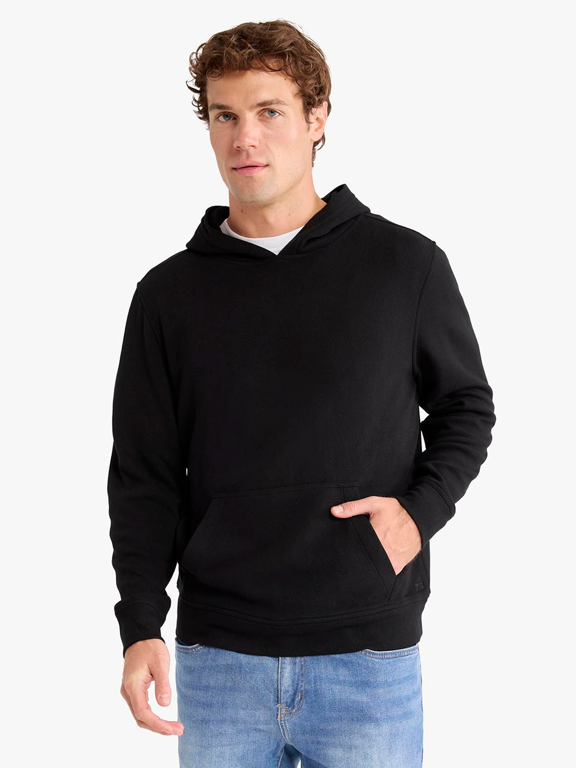 Man wearing black hooded blanket hoodie with front pocket, styled over white shirt and light blue jeans.
