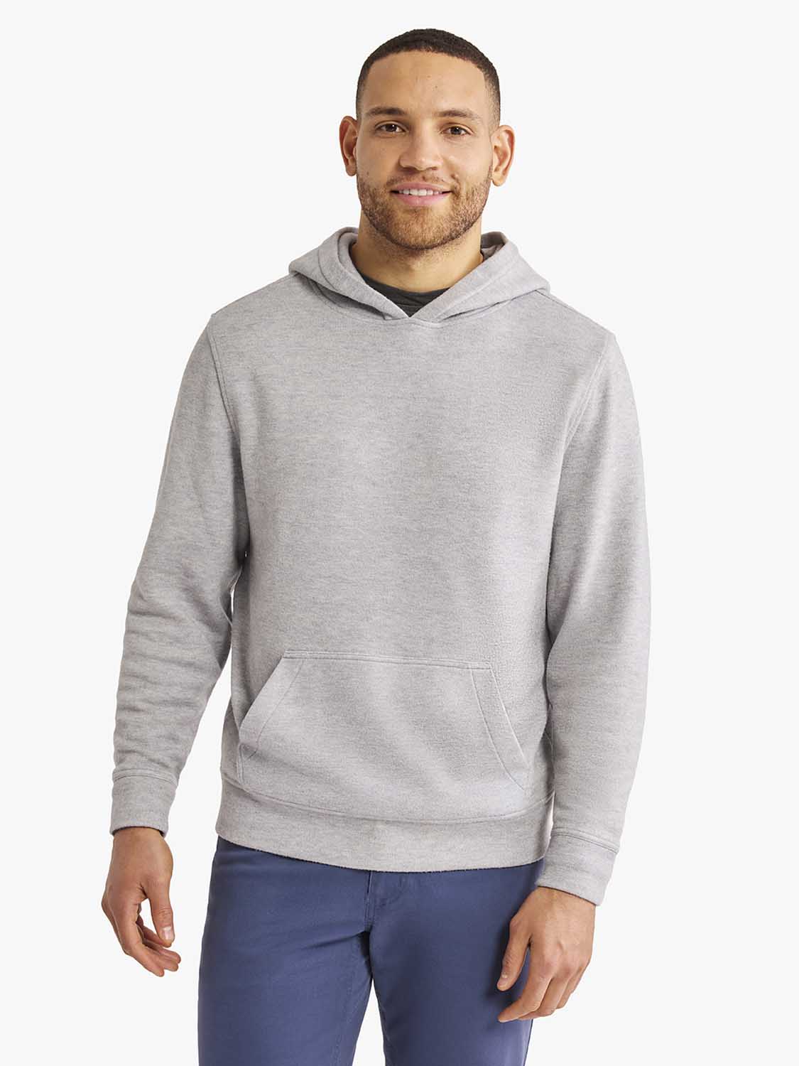 Man wearing a heather grey pullover hoodie with front pocket and navy blue pants.