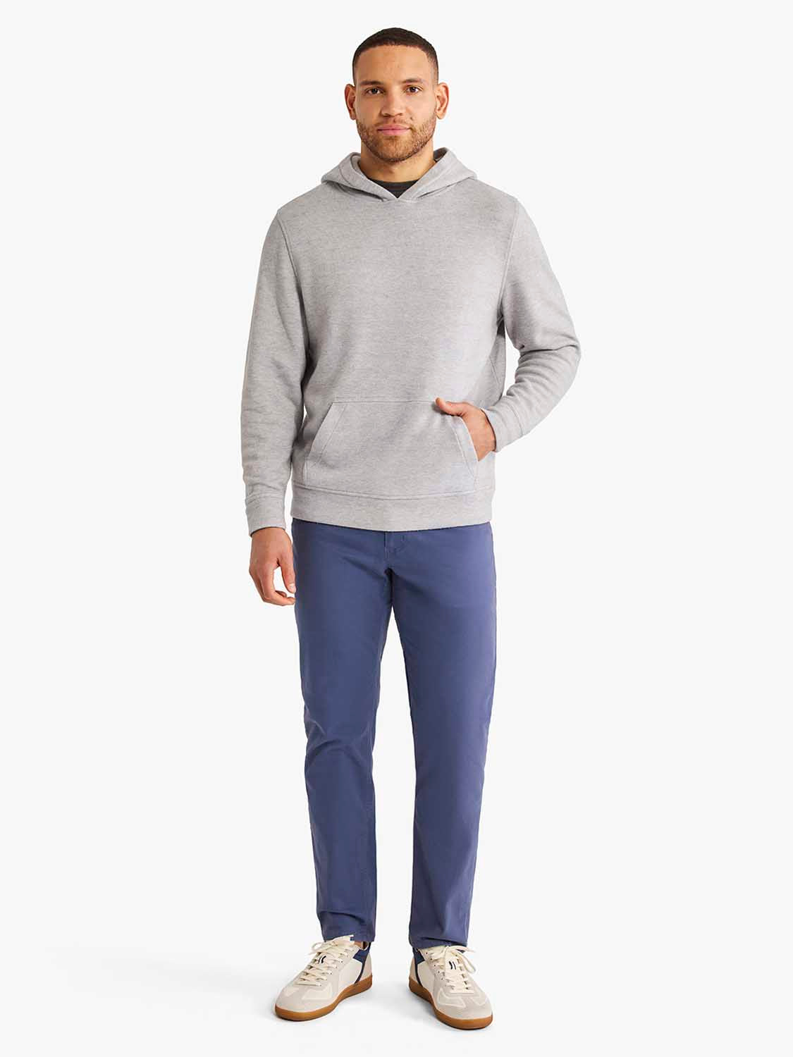 Man wearing a heather grey hoodie with front pockets and navy pants.