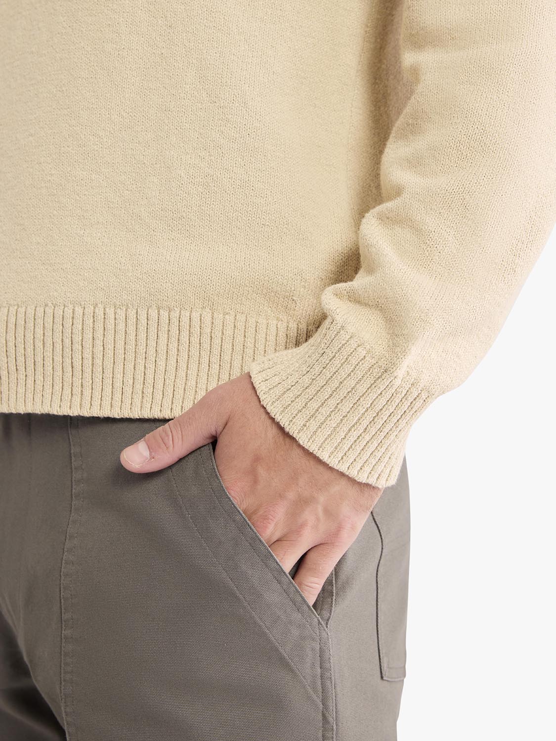 Beige crew neck sweater with ribbed cuffs worn with gray pants.