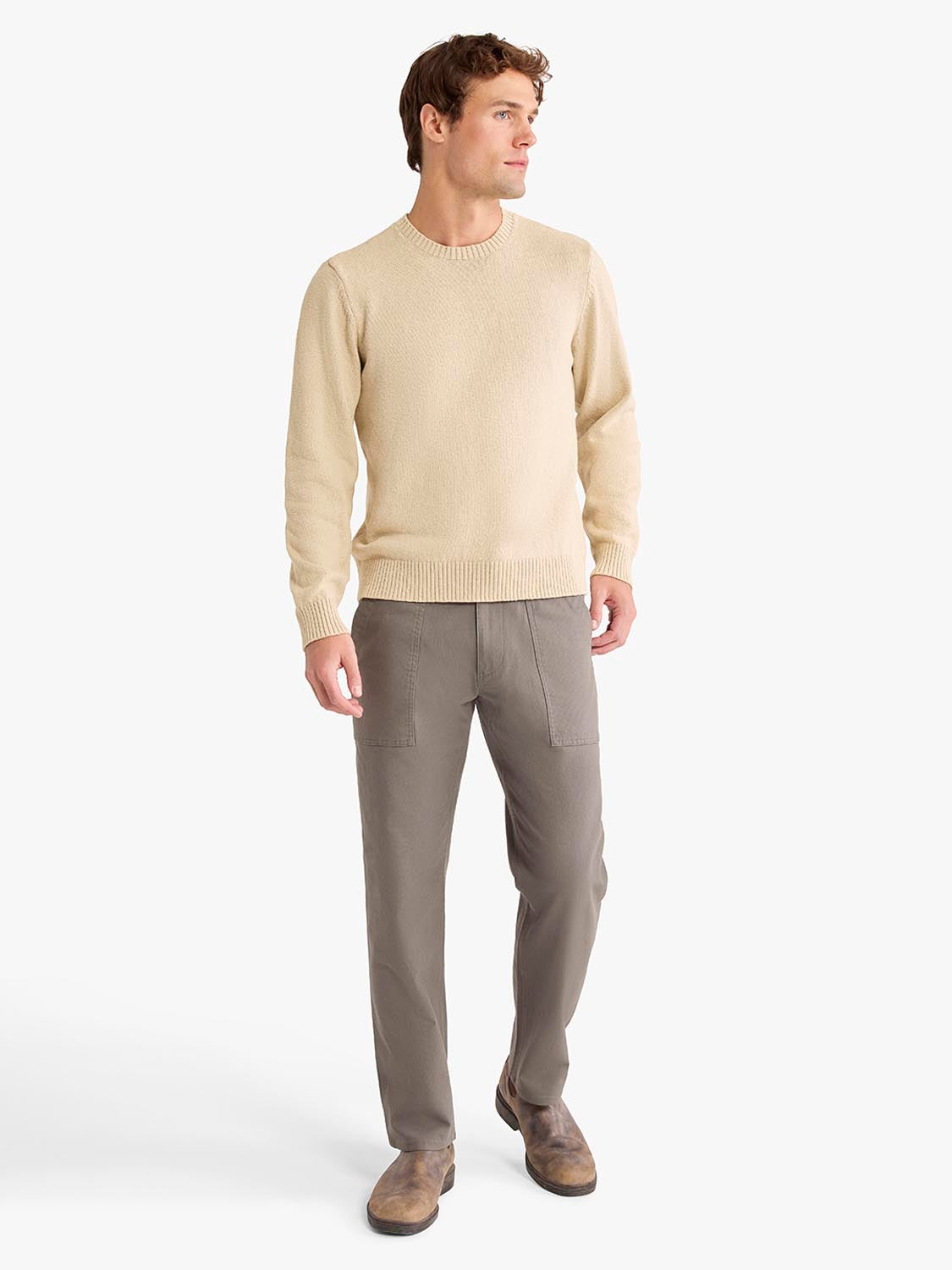 Man wearing a cream crew neck sweater with ribbed cuffs and gray pants with patch pockets.