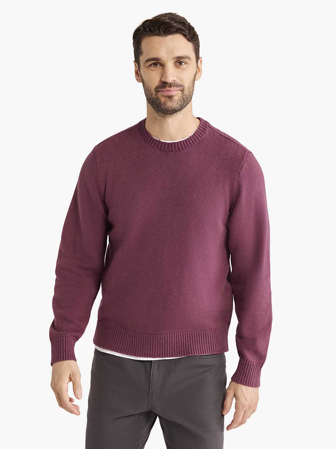 Man wearing a burgundy crew neck sweater with ribbed cuffs and hem over gray pants.